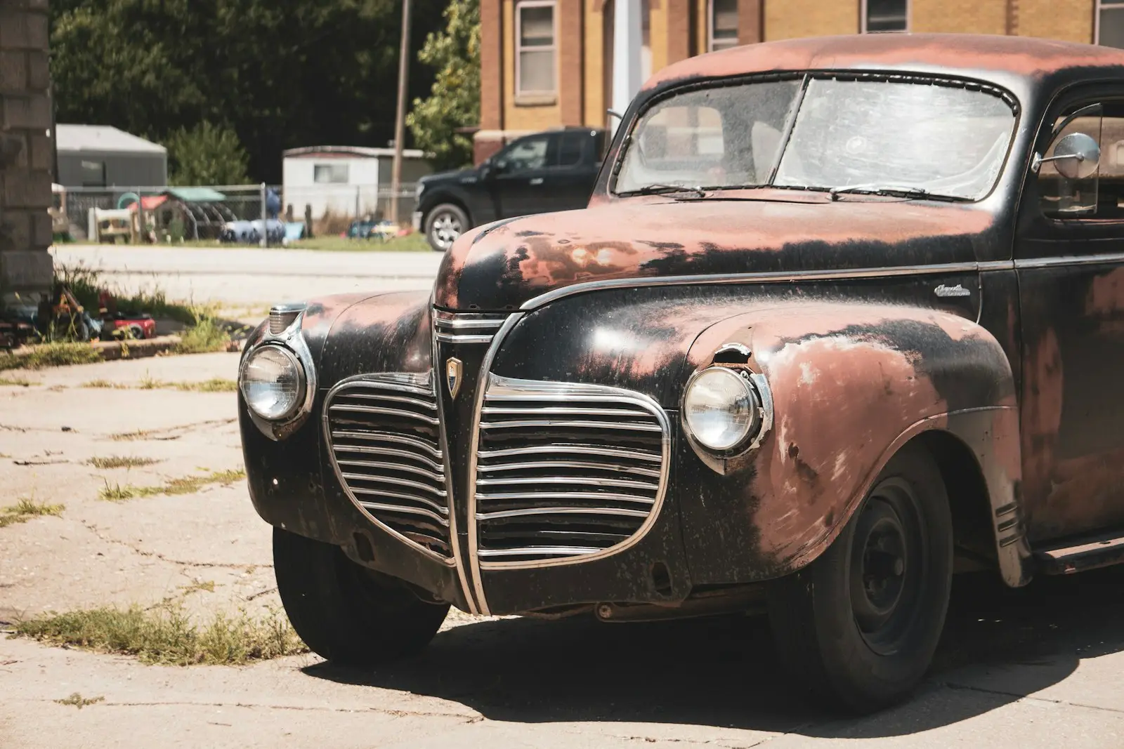 A rust-covered 1940s sedan parked at the edge of a cracked concrete lot